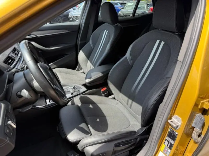 Intérieur avant du BMW X2 xDrive25eA 2021 en Galvanic Gold, sièges tissu gris avec bandes claires, vue côté conducteur ouverte.