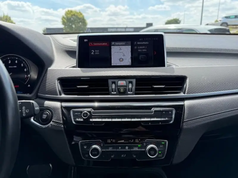 Tableau de bord du BMW X2 xDrive25eA 2021 avec écran central, commandes climatisation et finition noire moderne.