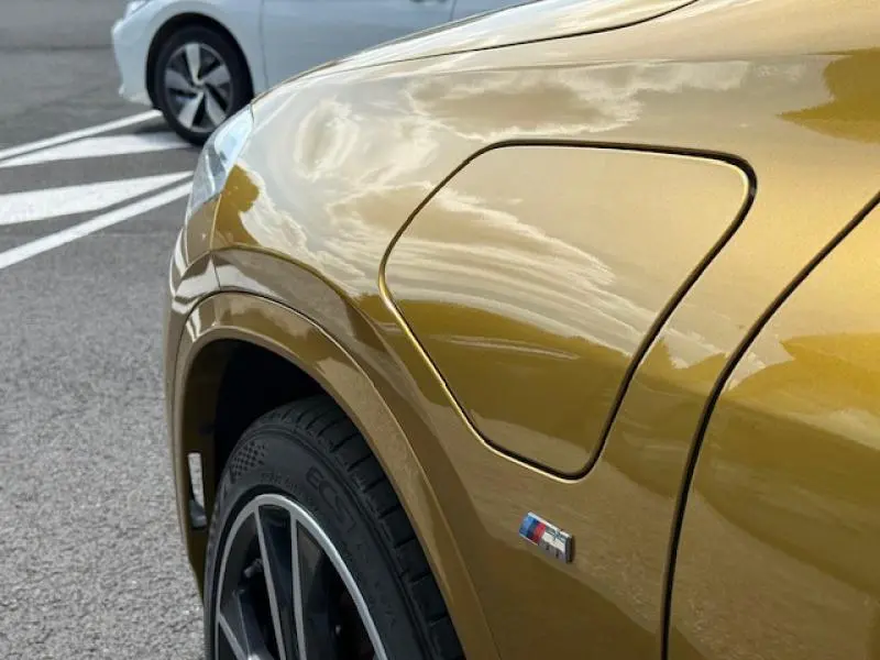 Détail de la trappe de recharge côté avant gauche d'un BMW X2 xDrive25eA 2021 en Galvanic Gold métallisé avec logo M Sport.
