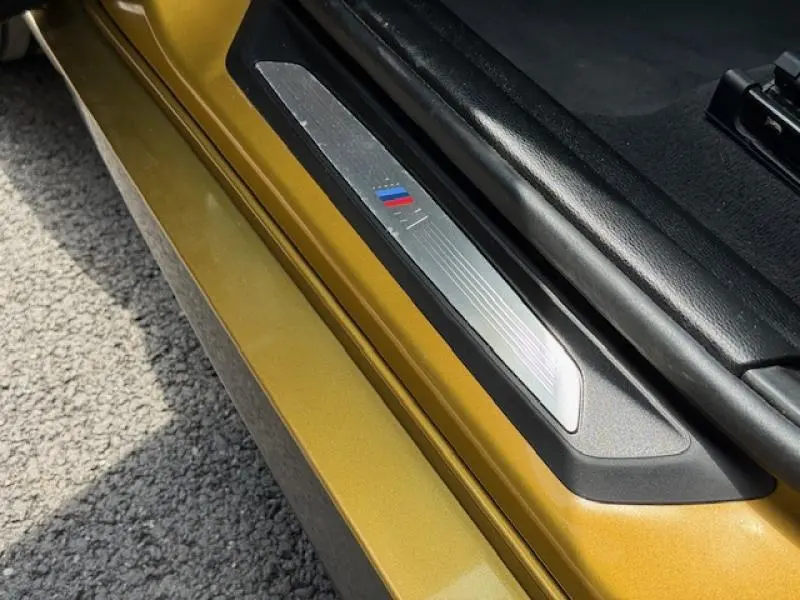 Gros plan sur le seuil de porte côté gauche d'un BMW X2 Galvanic Gold métallisé avec logo M Sport visible.