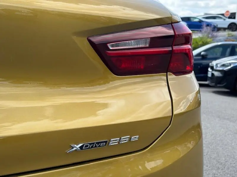 Gros plan sur l'arrière droit d'un BMW X2 hybride rechargeable en Galvanic Gold métallisé avec feu arrière et badge xDrive 25e.