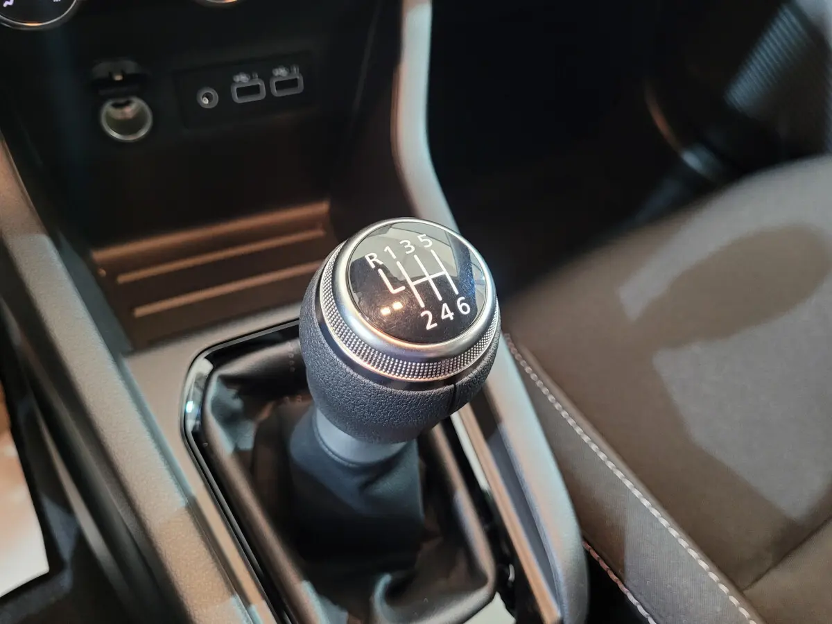 Gros plan sur le levier de vitesse manuel de la Renault Clio gris foncé, avec console centrale et siège tissu visibles.