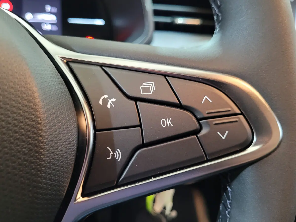 Gros plan sur les commandes noires du volant cuir synthétique de la Renault Clio gris foncé, boutons multifonctions visibles.