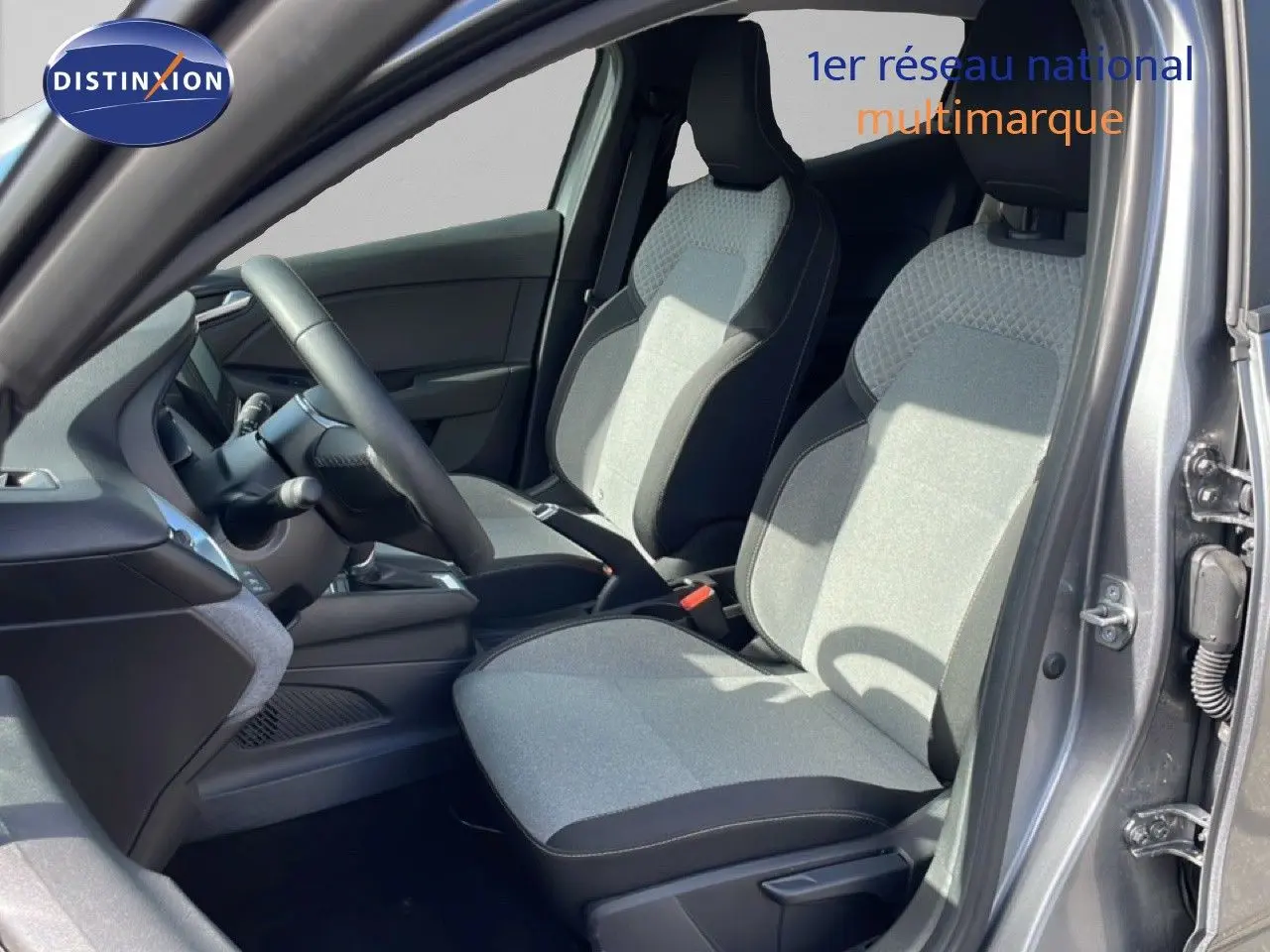 Vue intérieure côté conducteur de la Renault Clio gris schiste métal, sièges tissu bicolore et volant cuir multifonction.
