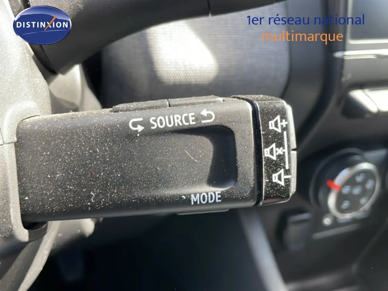 Gros plan sur la commande au volant de la Renault Clio 2025, bouton source et mode, intérieur noir.