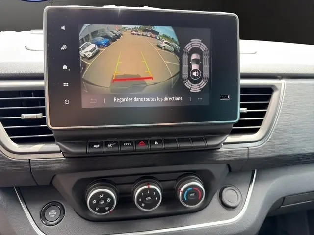 Vue intérieure du tableau de bord du Nissan Primastar 2025 avec écran tactile affichant la caméra de recul et commandes climatisation.