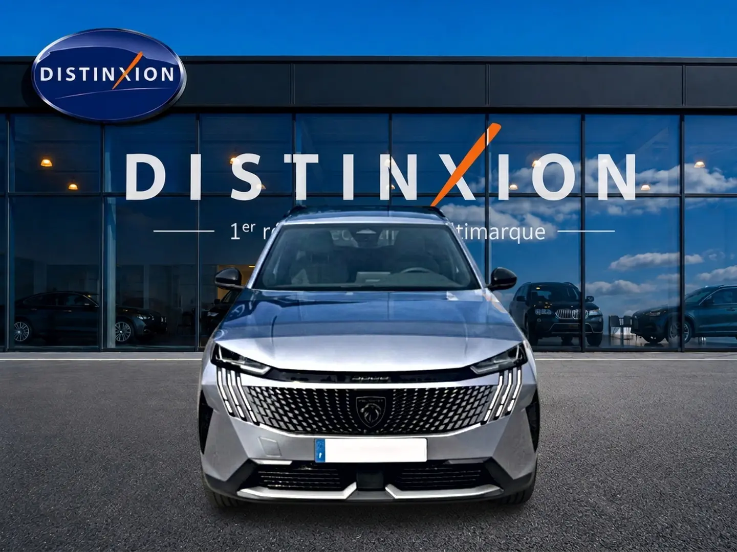 Vue frontale d'un Peugeot 5008 Hybrid 145 allure e-dcs6 gris artense devant une vitrine Distinxion.
