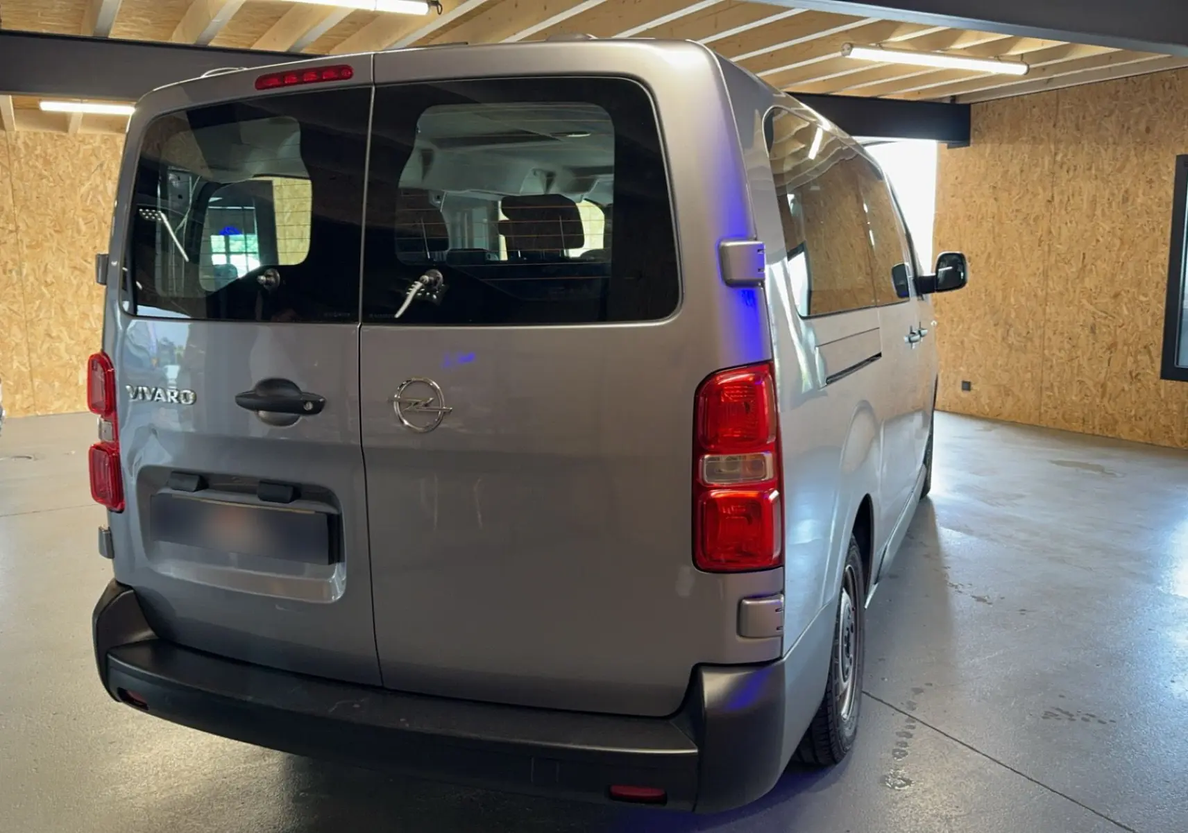 Vue 3/4 arrière d'un Opel Vivaro Combi gris 2022 avec portes arrière vitrées et feux rouges visibles.