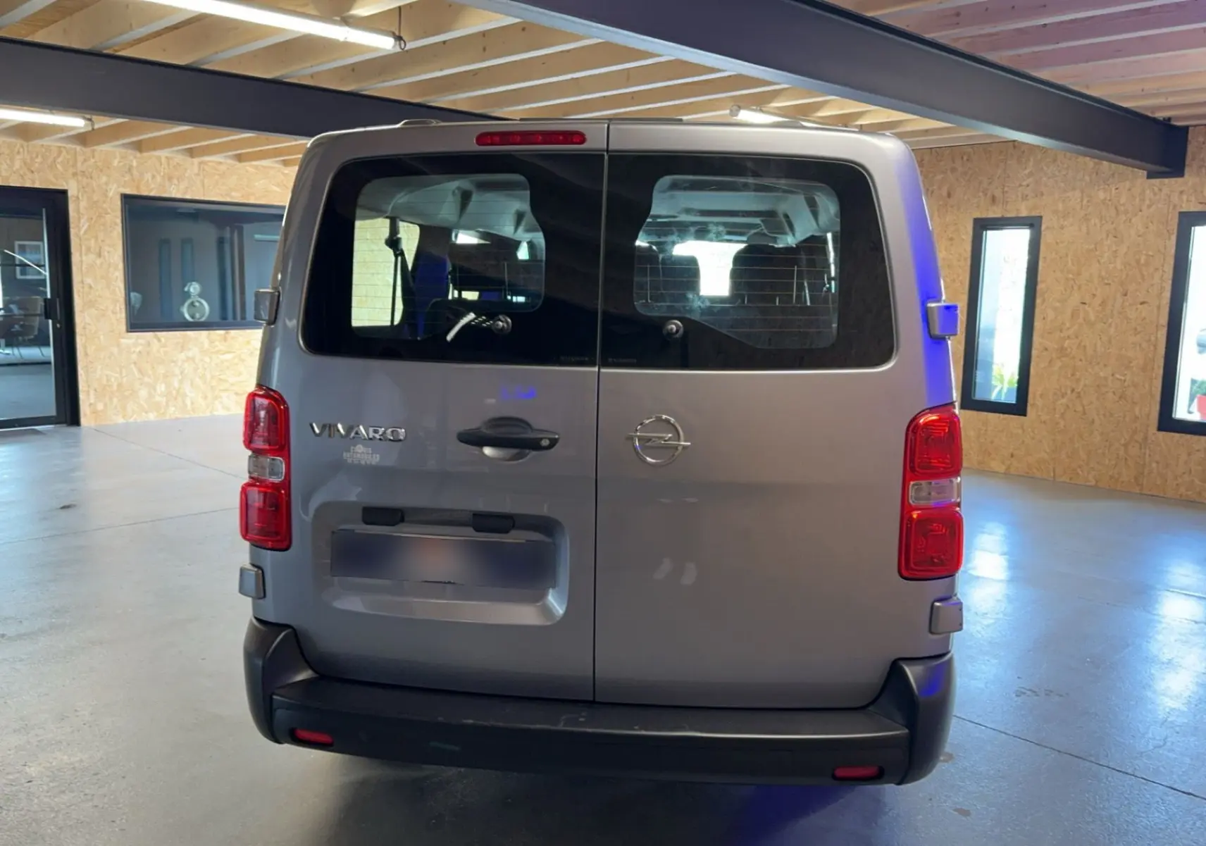 Vue arrière d'un Opel Vivaro Combi gris 2022 avec portes battantes et feux arrière rouges dans un garage.