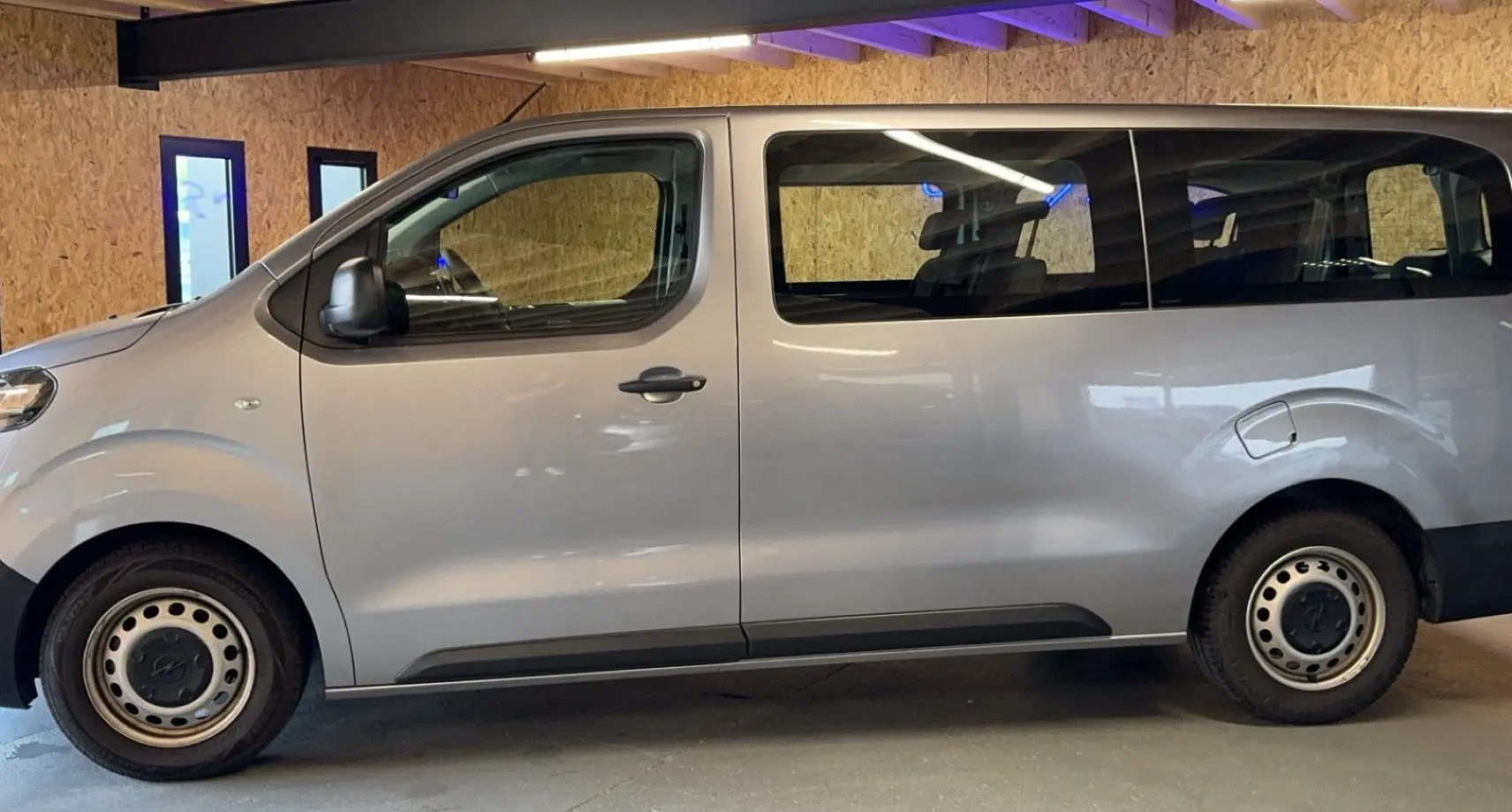 Profil côté gauche d'un Opel Vivaro Combi gris 2022 avec jantes acier et grandes fenêtres teintées.