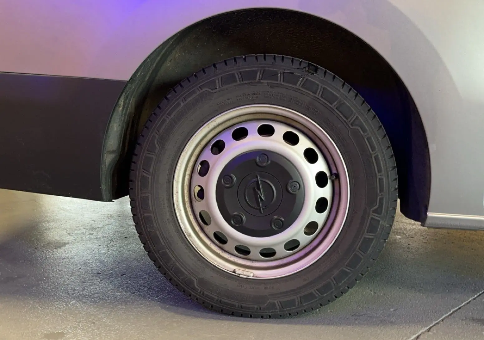 Gros plan sur la roue avant gauche d'un Opel Vivaro Combi gris 2022 avec jante acier et logo Opel central.