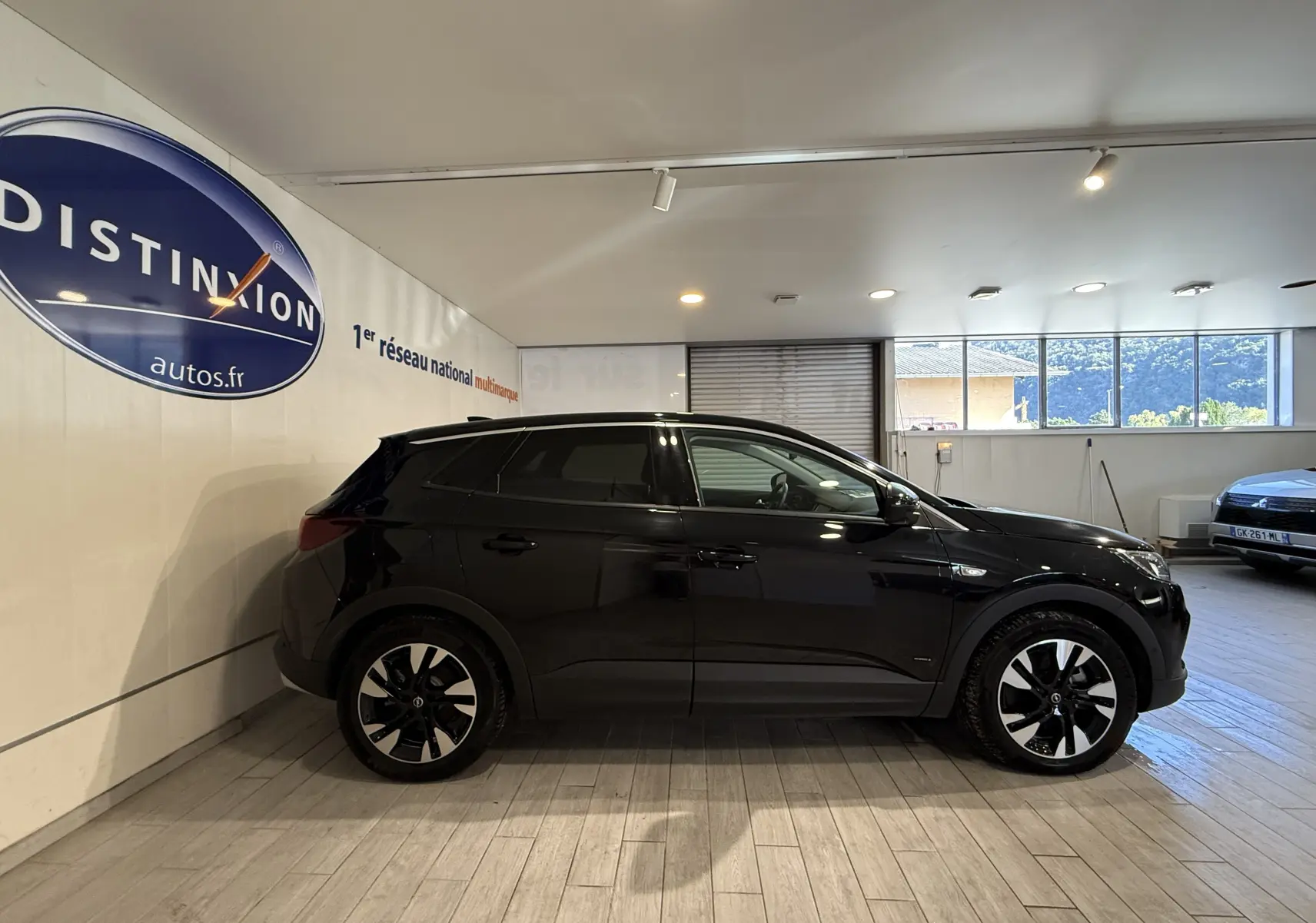 Profil côté gauche d'un Opel Grandland X noir métal, hybride rechargeable, en intérieur avec jantes noires et argentées.