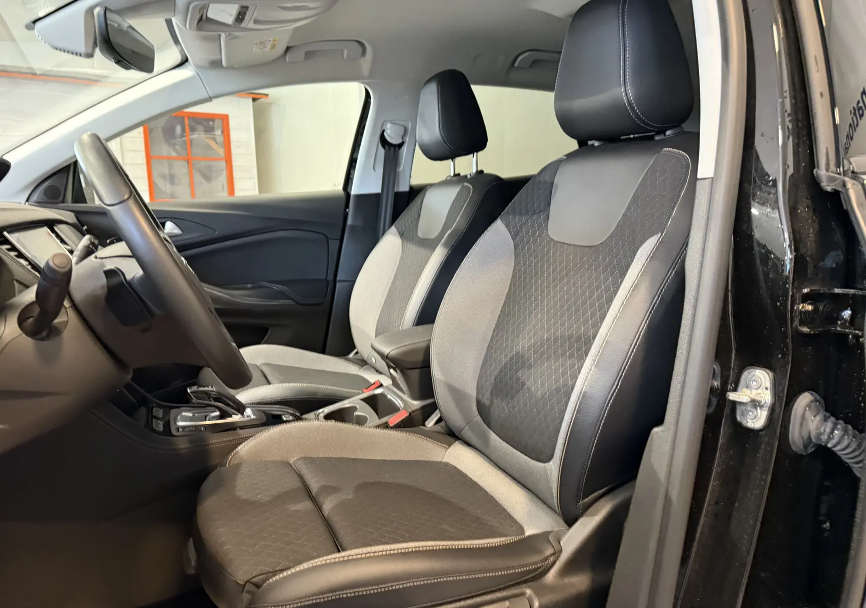 Vue intérieure côté conducteur de l'Opel Grandland X noir métal, montrant les sièges avant en tissu et cuir bicolore.
