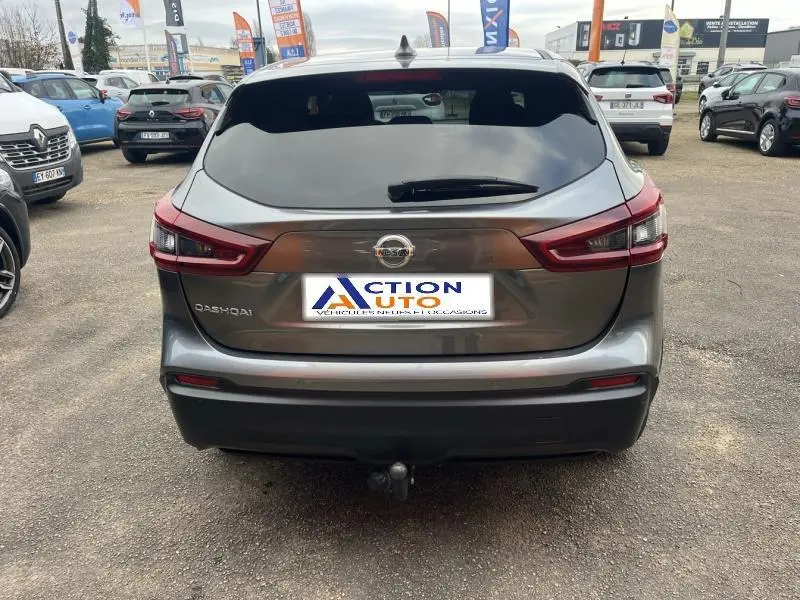 Vue arrière d'un Nissan Qashqai gris Squale avec hayon fermé et attelage visible sur un parking.