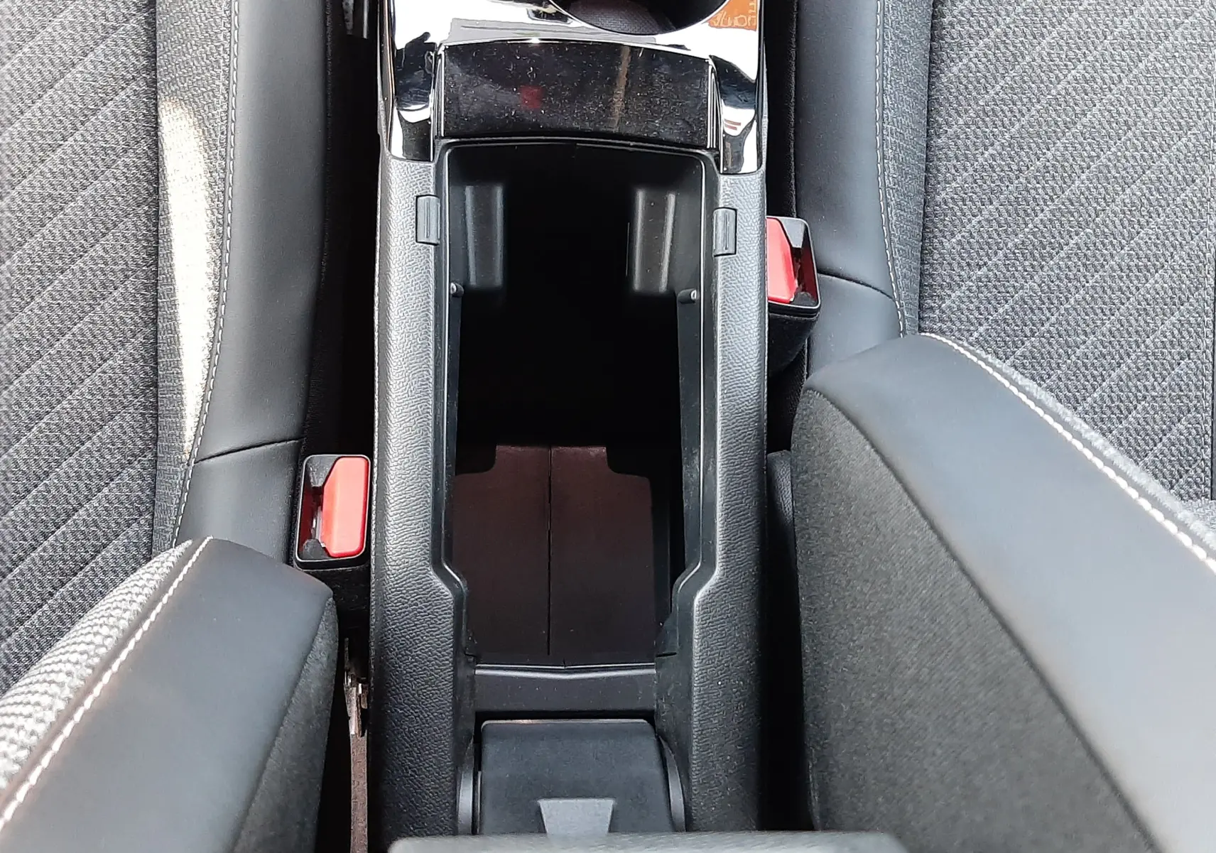 Vue plongeante sur la console centrale ouverte de la Peugeot 2008 Hybrid 145 Allure avec sièges gris et accoudoirs noirs.