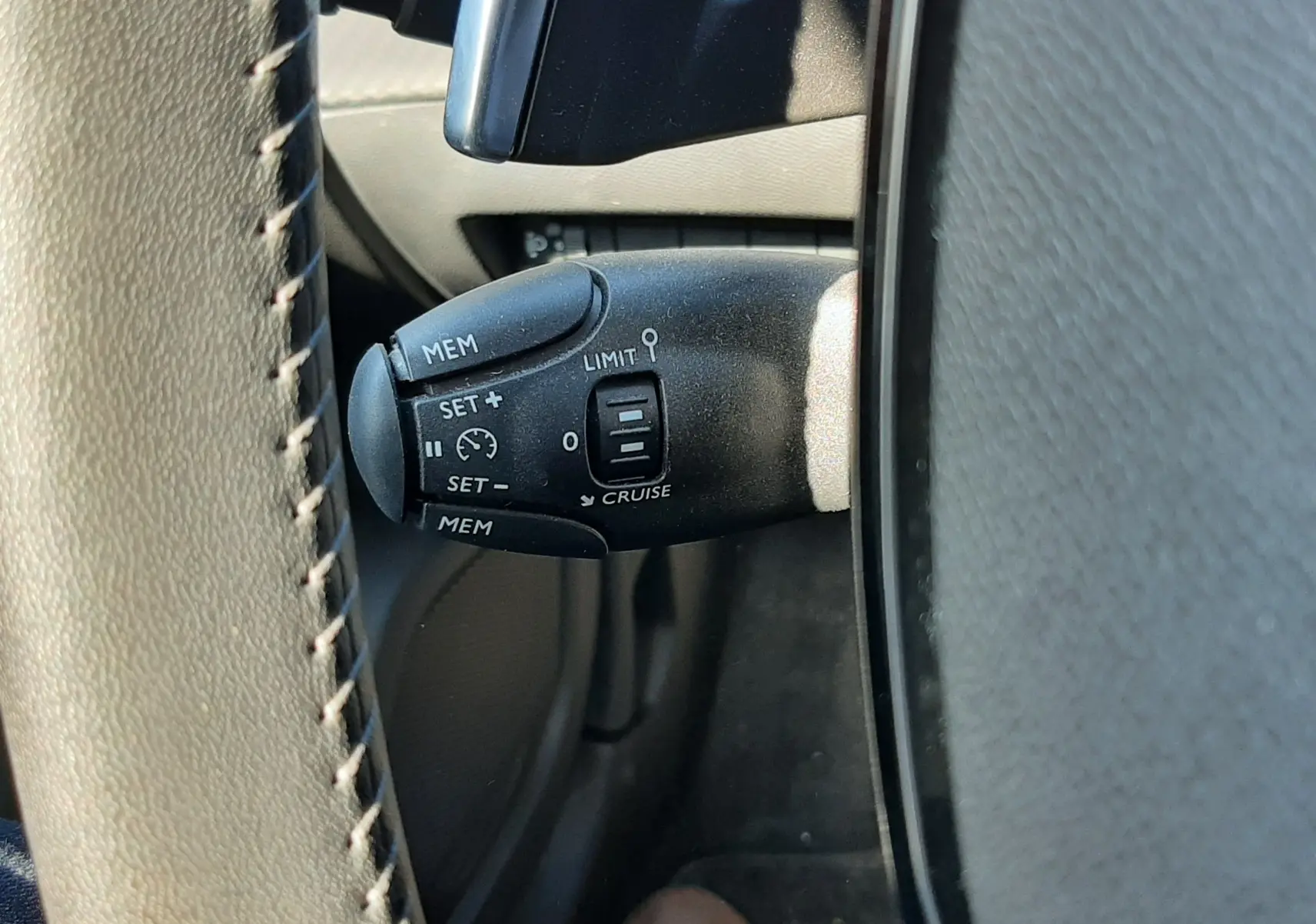 Gros plan sur la commande de régulateur de vitesse noire à gauche du volant gris du Peugeot 2008 Hybrid 145 Allure.