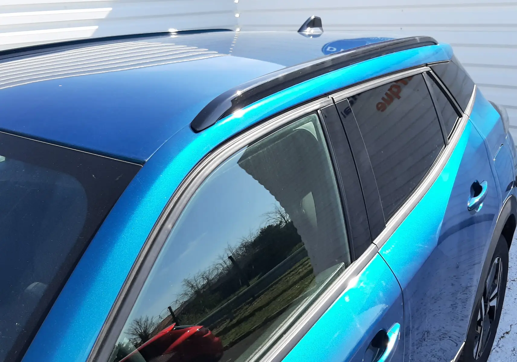 Vue 3/4 arrière côté droit du Peugeot 2008 Hybrid 145 Allure en bleu Obsession avec barres de toit noires.