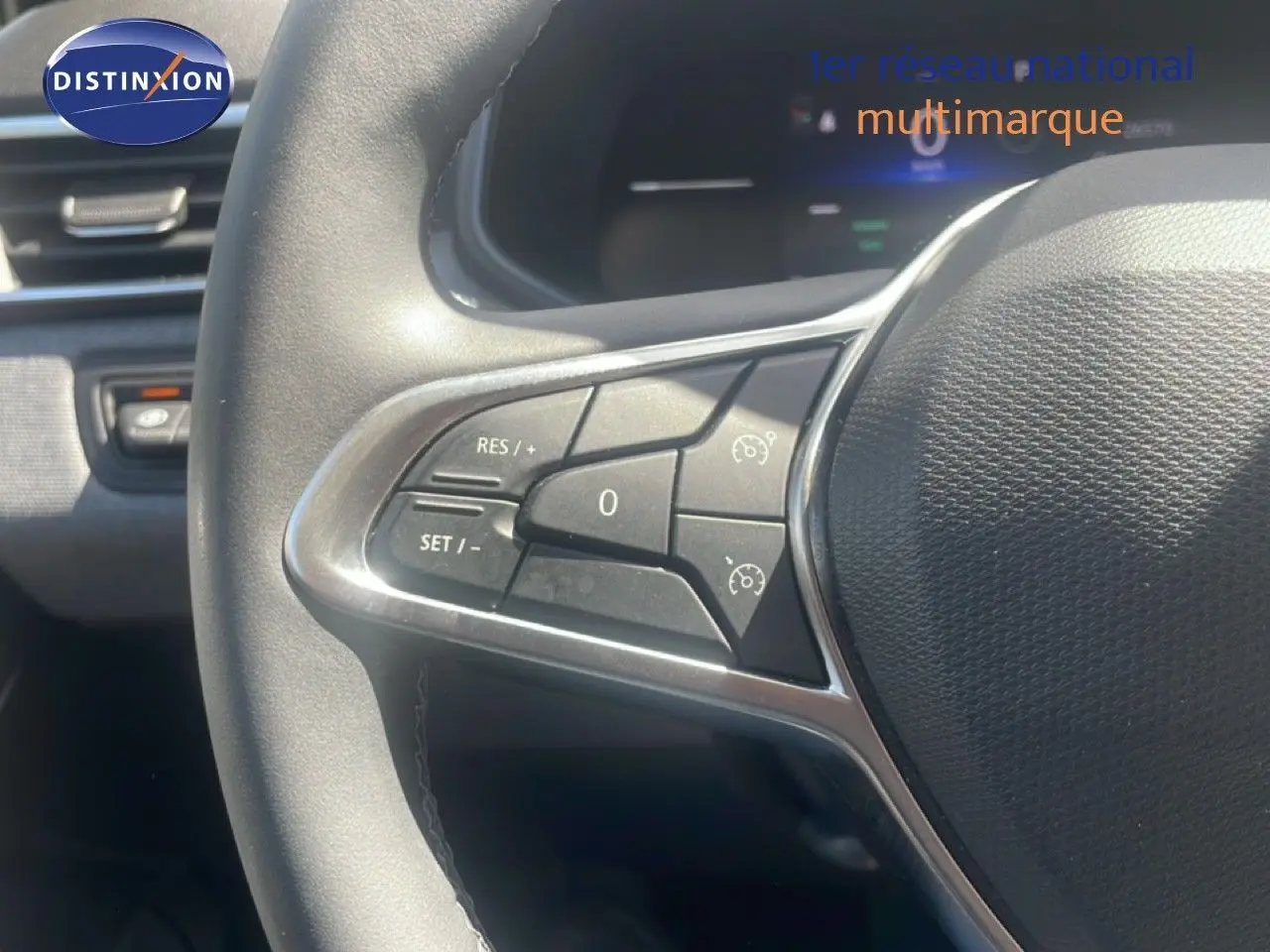 Gros plan sur les commandes au volant côté gauche de la Renault Clio blanche, mettant en valeur les boutons de régulateur de vitesse.