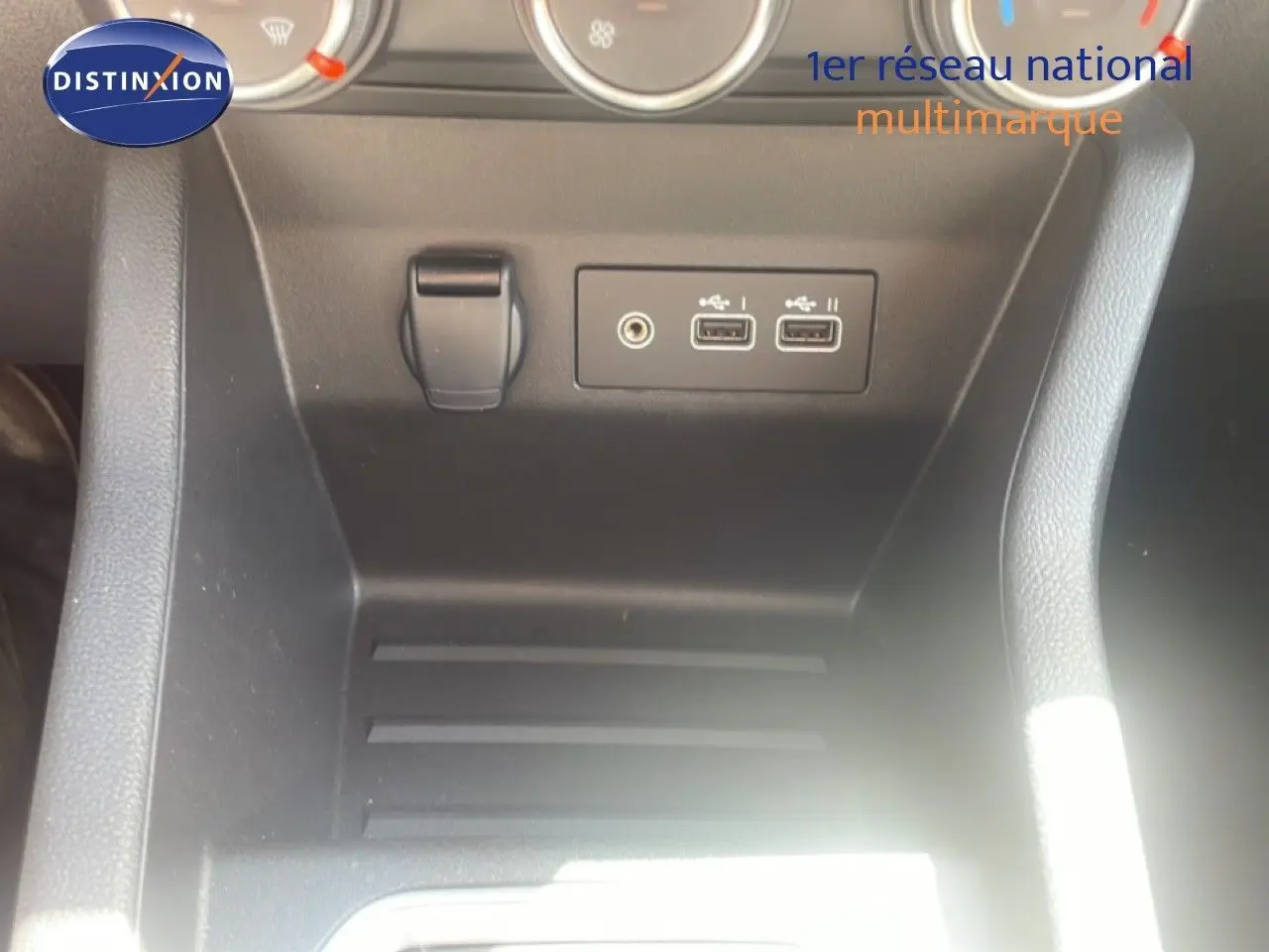 Vue rapprochée de la console centrale noire de la Renault Clio blanche, montrant les ports USB et la prise auxiliaire.
