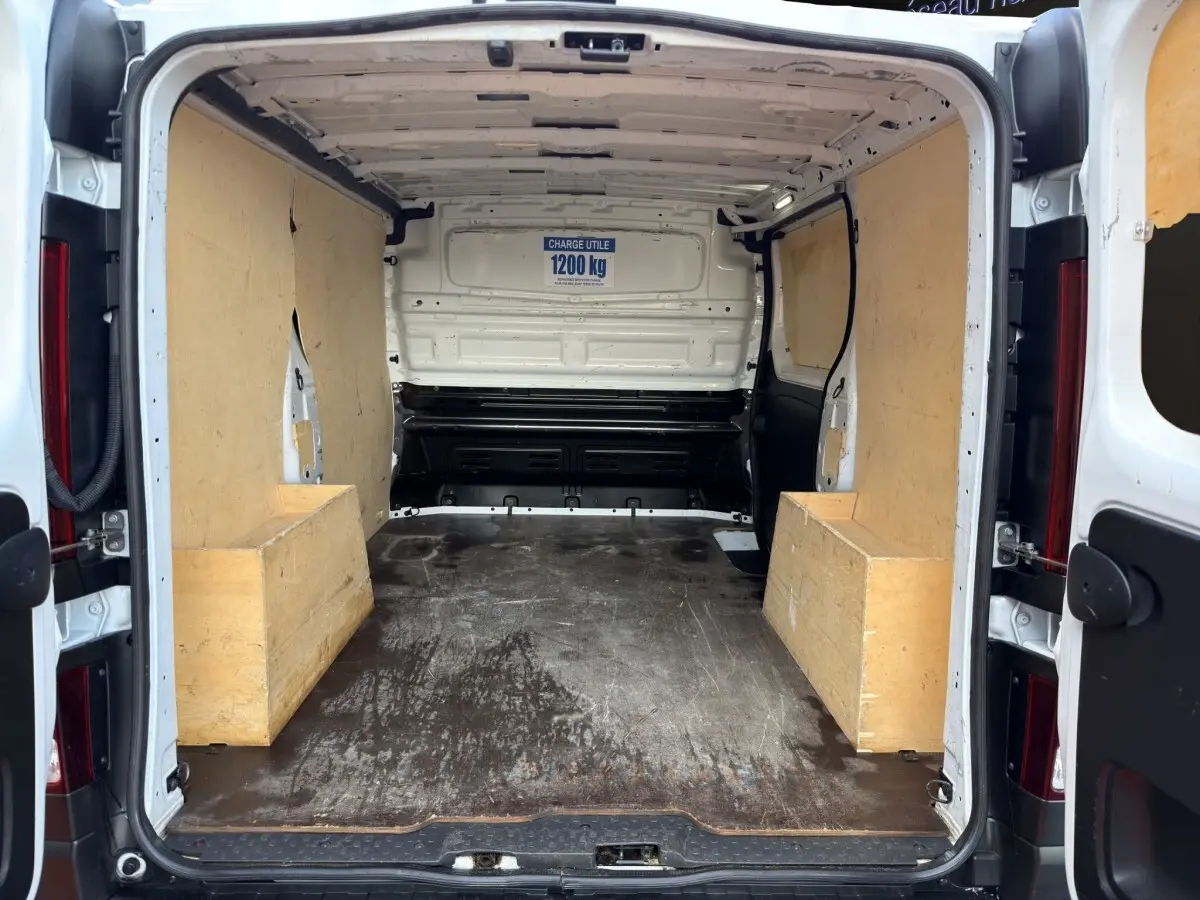 Vue arrière du fourgon Renault Trafic blanc 2024, montrant l’espace de chargement avec protections en bois sur les côtés.