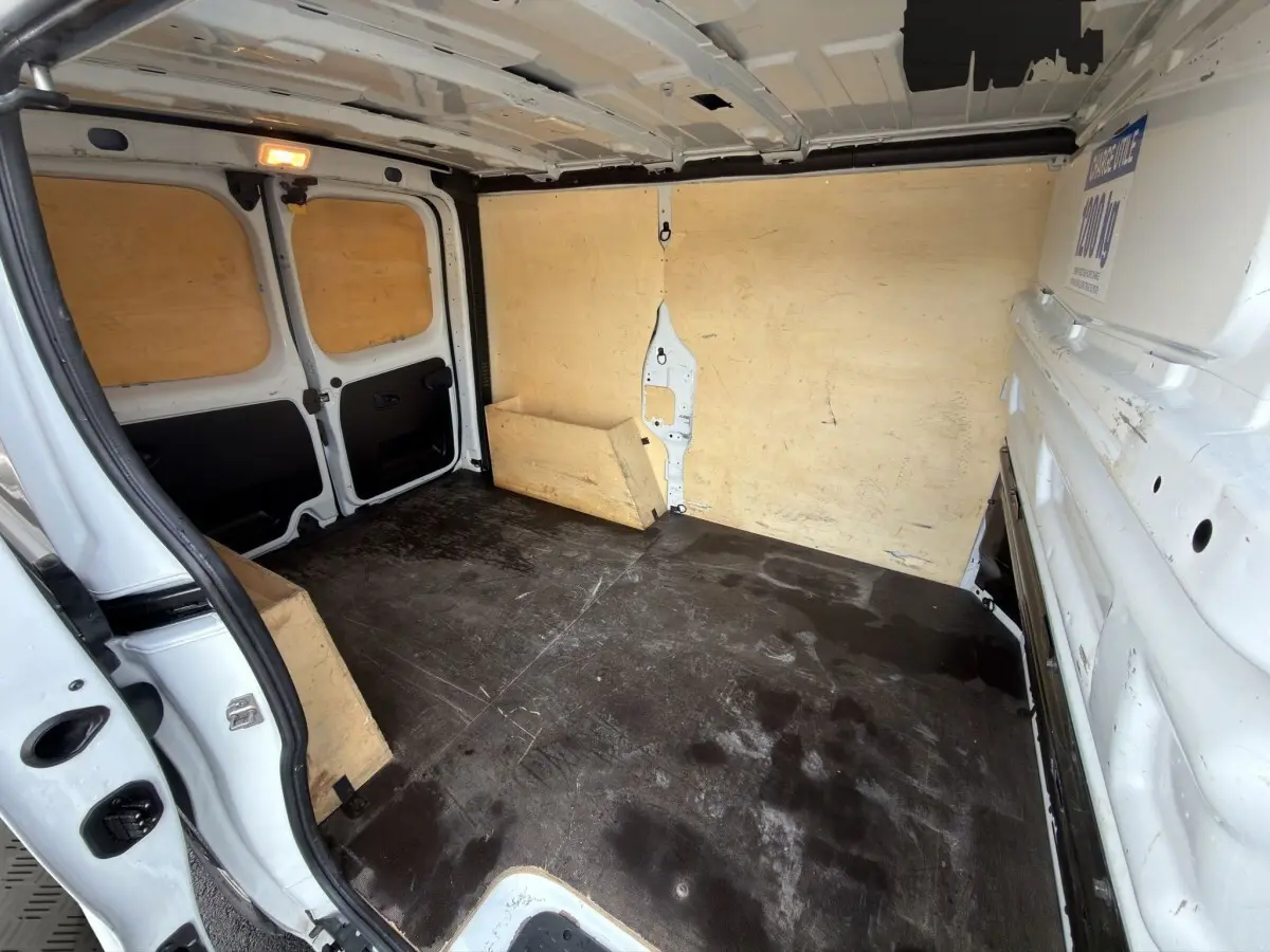 Vue intérieure arrière du fourgon blanc Renault Trafic avec cloison et plancher en bois, montrant l'espace de chargement vide.