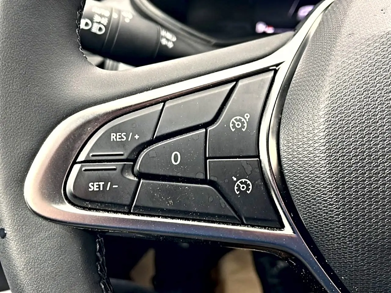 Gros plan sur les commandes de régulateur de vitesse au volant noir de la Renault Clio V blanche.