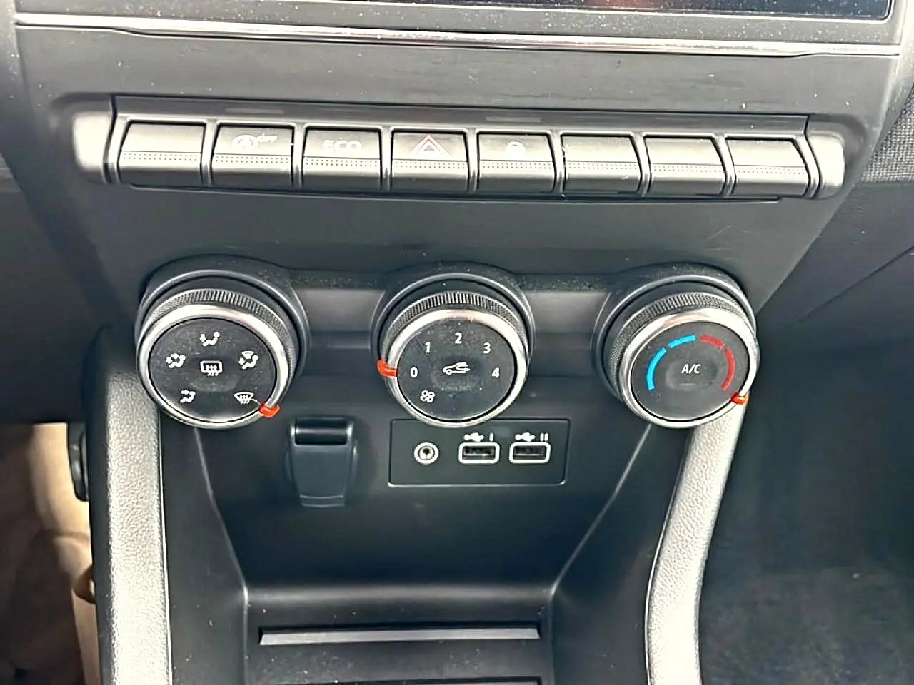 Gros plan sur les commandes de climatisation et les ports USB du tableau de bord d'une Renault Clio V blanche.