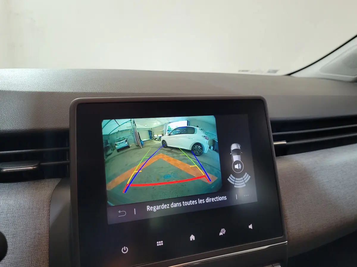 Écran central montrant la caméra de recul avec vue arrière d’un véhicule blanc dans un garage, intérieur Renault Clio gris.