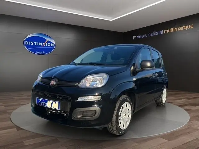 Vue 3/4 avant d'une FIAT Panda noire 2025 en showroom, avec phares arrondis et jantes blanches.