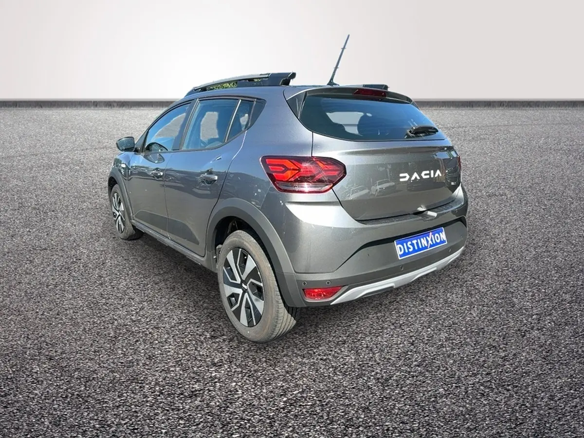 Vue 3/4 arrière droite d'une Dacia Sandero Stepway gris foncé avec barres de toit et jantes distinctives.