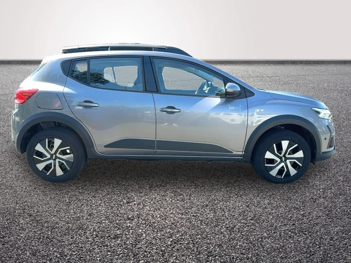 Profil droit d'une Dacia Sandero Stepway gris foncé avec barres de toit et jantes distinctives sur sol gravillonné.