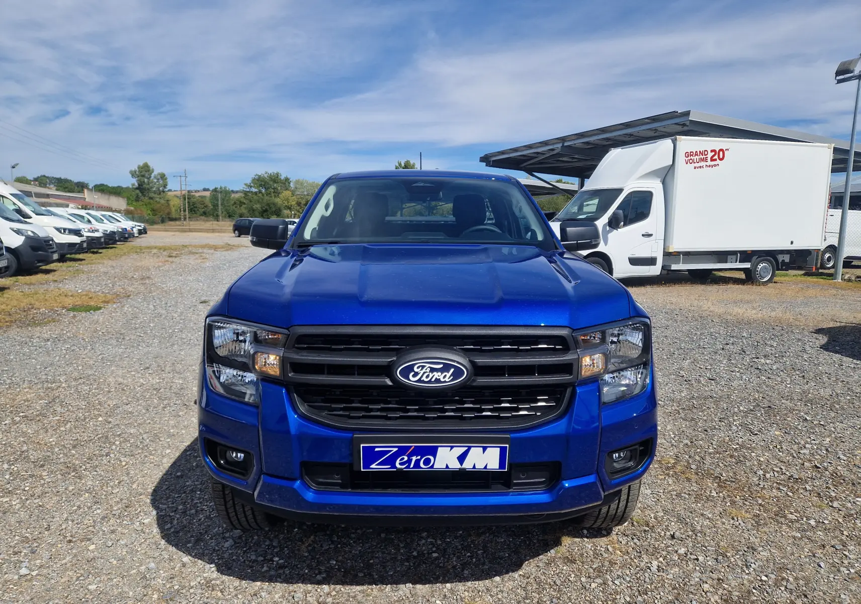 Vue de face du Ford Ranger Super Cabine bleu Lightning avec calandre noire et plaque "Zero KM" sur un parking extérieur.