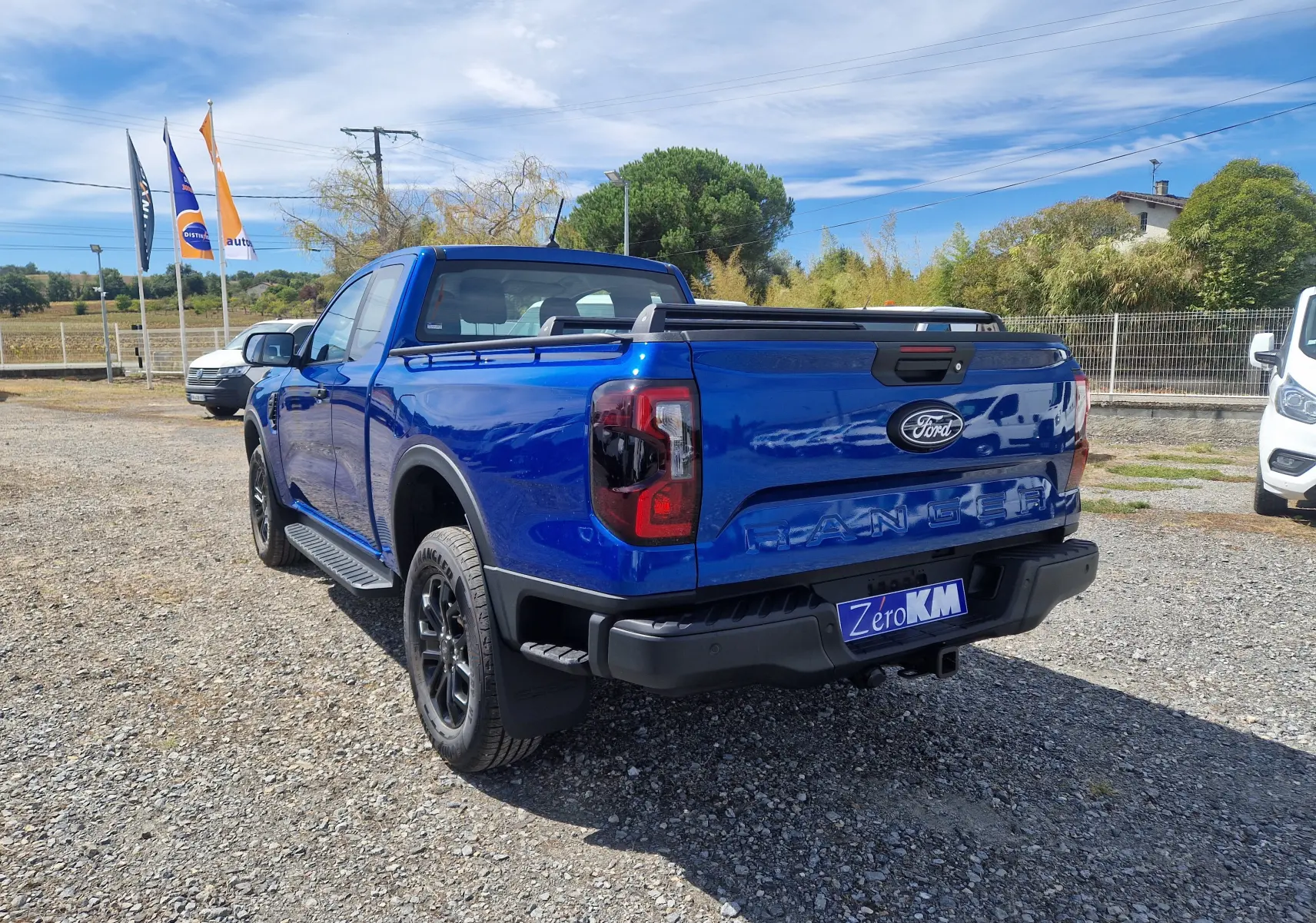 Vue 3/4 arrière droite d'un Ford Ranger Super Cabine bleu Lightning avec rideau de plateau rigide et barres sur plateau.
