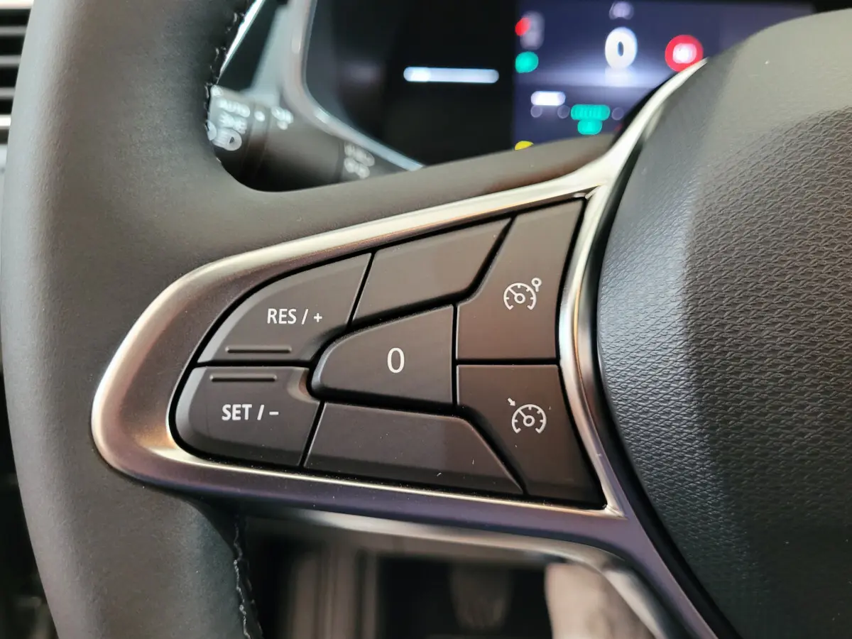 Gros plan sur les commandes du régulateur de vitesse au volant cuir de la Renault Clio gris foncé, tableau de bord en arrière-plan flou.