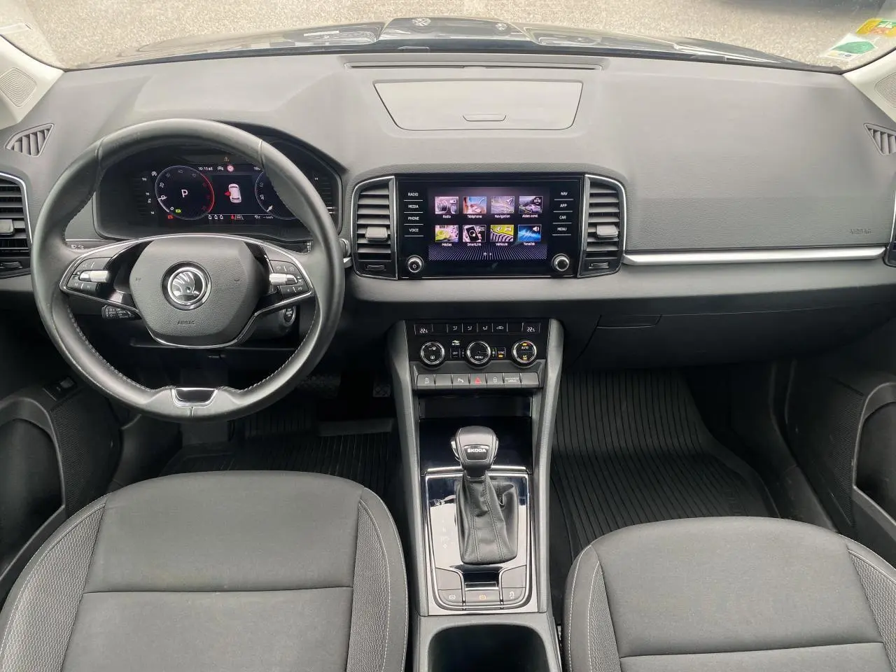 Vue intérieure frontale du tableau de bord et volant noir du Skoda Karoq gris graphite 2022 avec écran tactile central.