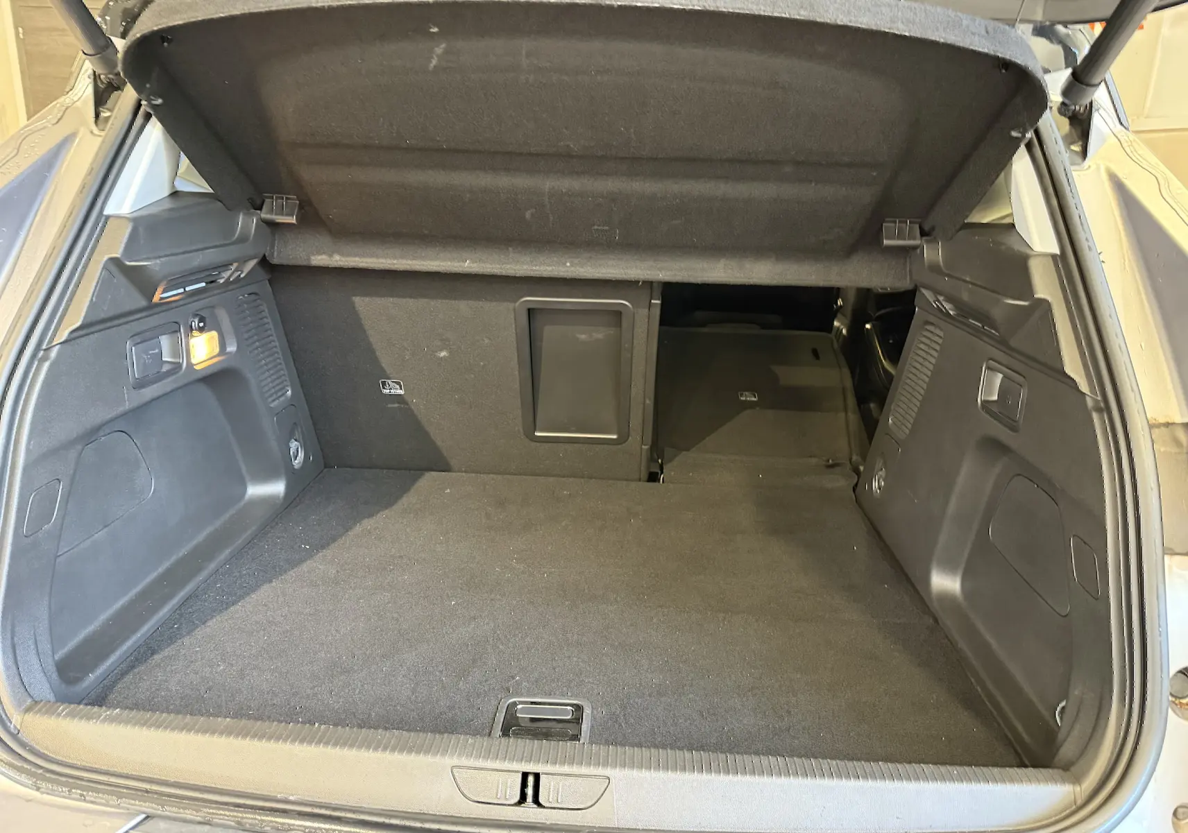 Coffre ouvert vu de l'arrière d'un Opel Grandland X gris Himalaya, espace de chargement spacieux et tapis noir.
