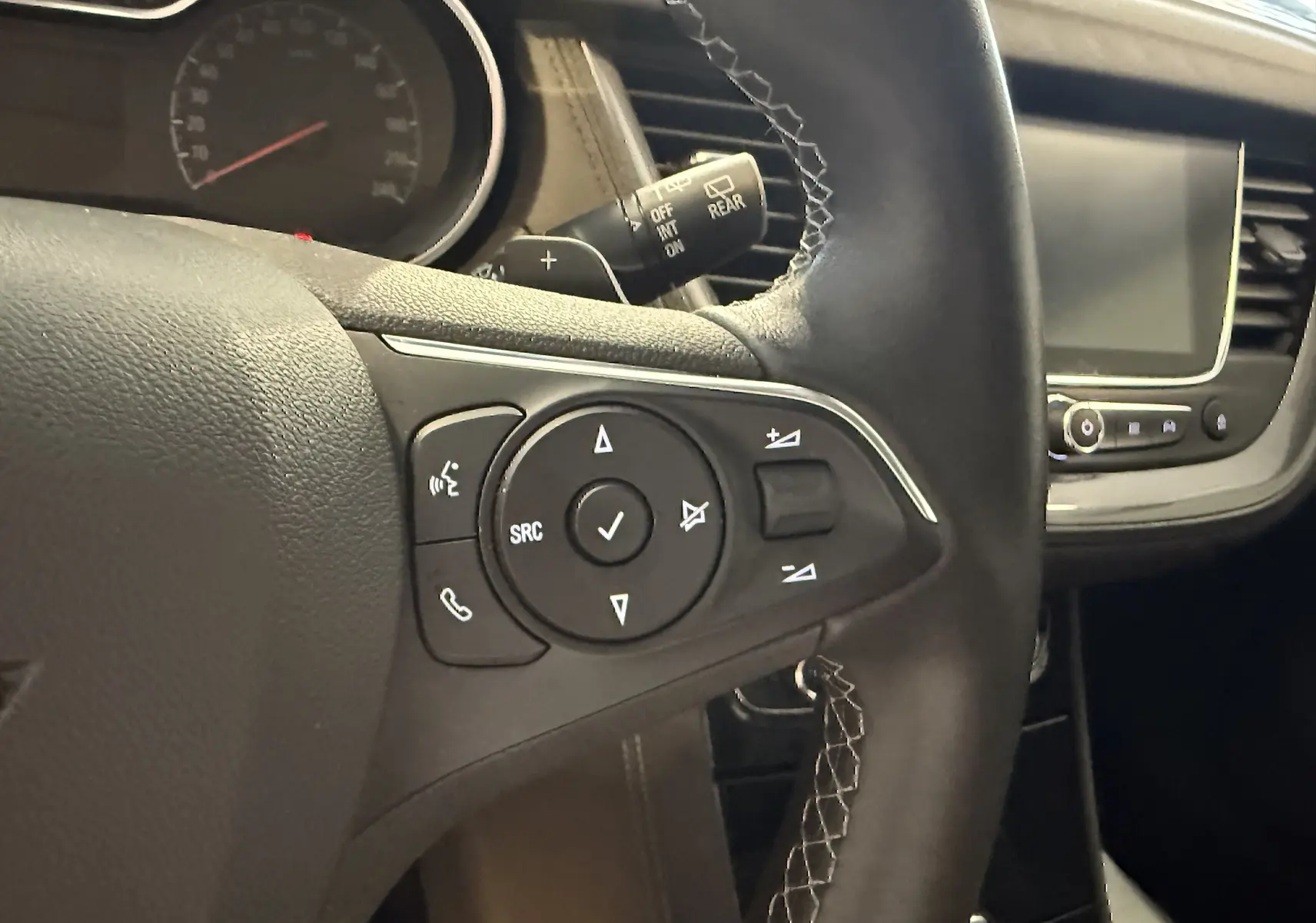 Gros plan sur le volant gauche de l’Opel Grandland X gris Himalaya, avec commandes audio et écran tactile visible.