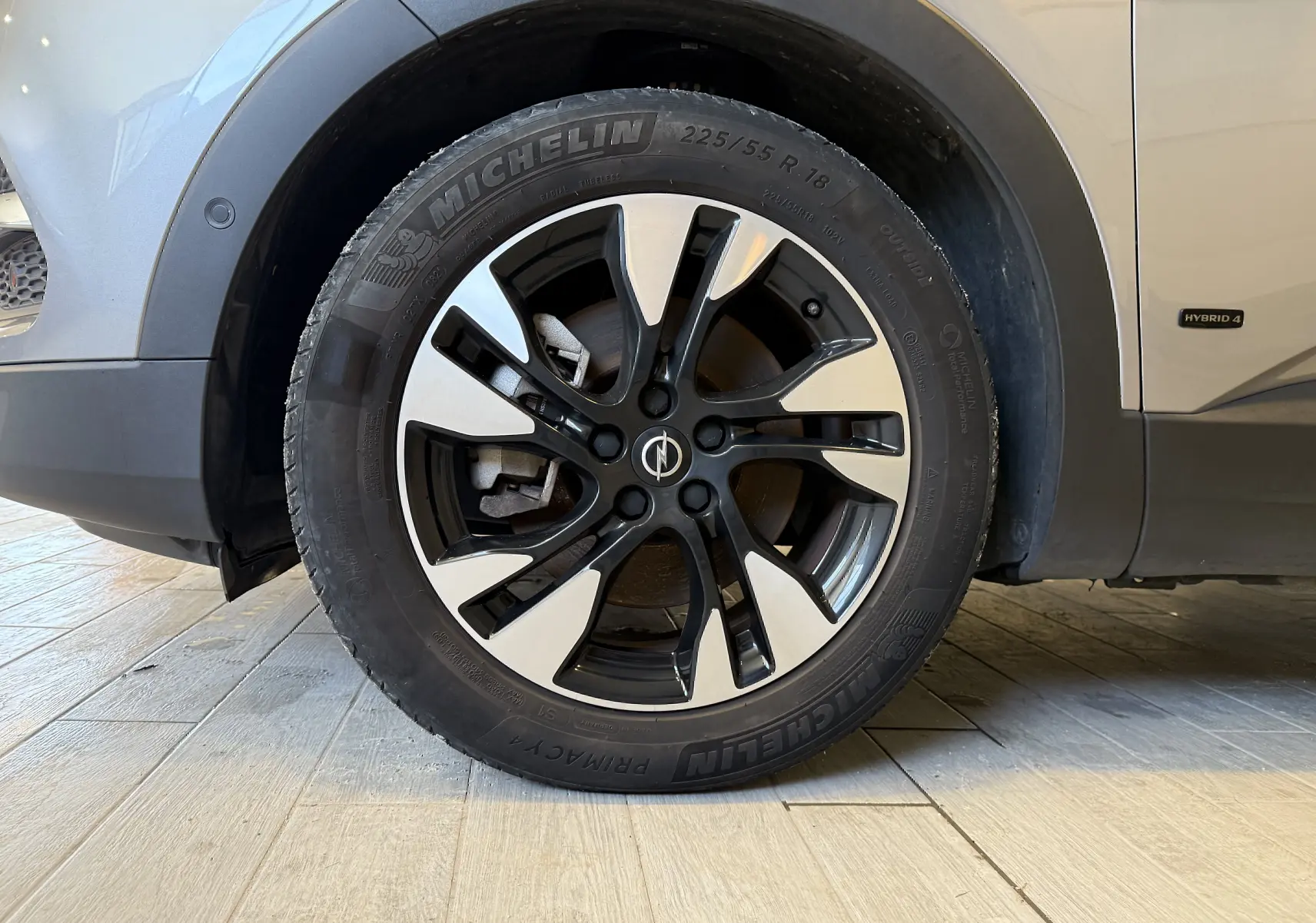 Gros plan sur la roue avant gauche d'un Opel Grandland X gris Himalaya avec jante alliage bicolore et badge Hybrid 4 visible.