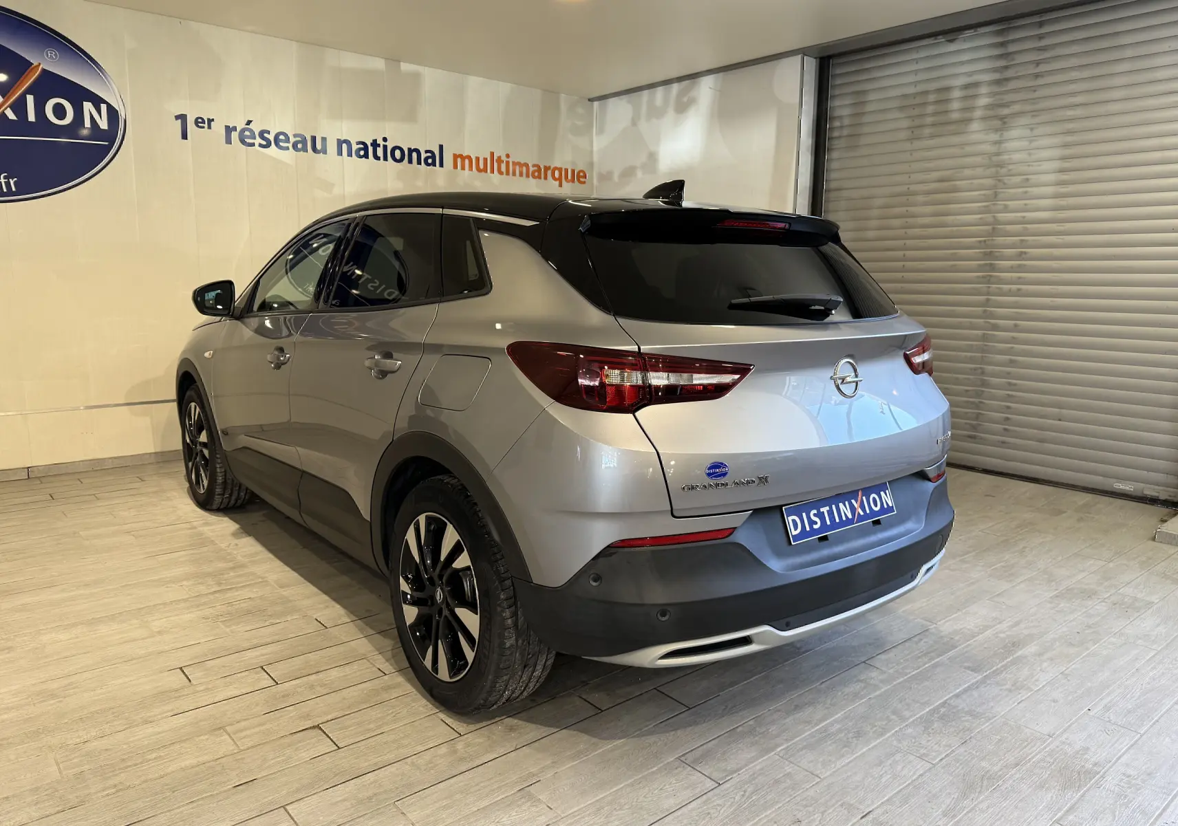 Opel Grandland X gris Himalaya métal vu en 3/4 arrière droit dans un showroom avec jantes noires et toit noir.