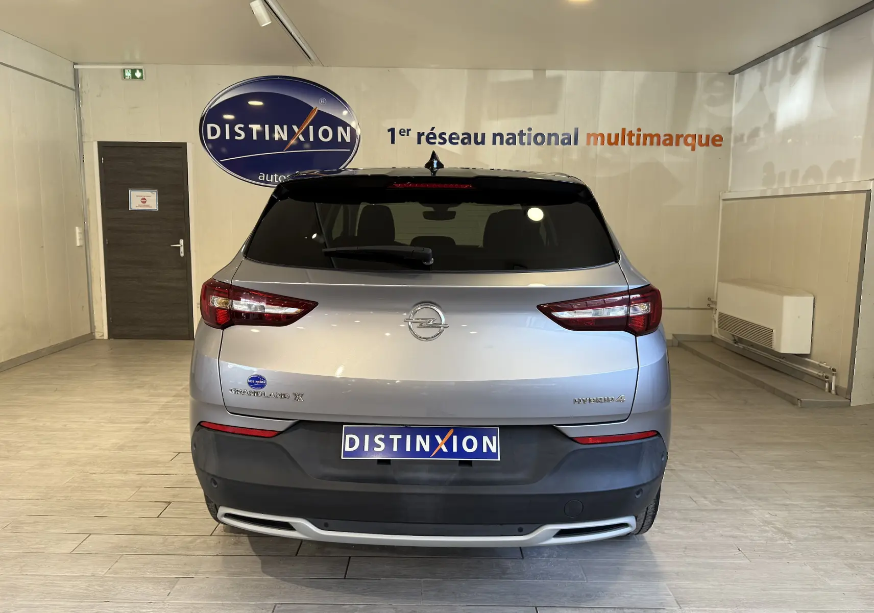 Vue arrière d'un Opel Grandland X gris Himalaya métal avec logo Distinxion dans un showroom lumineux.