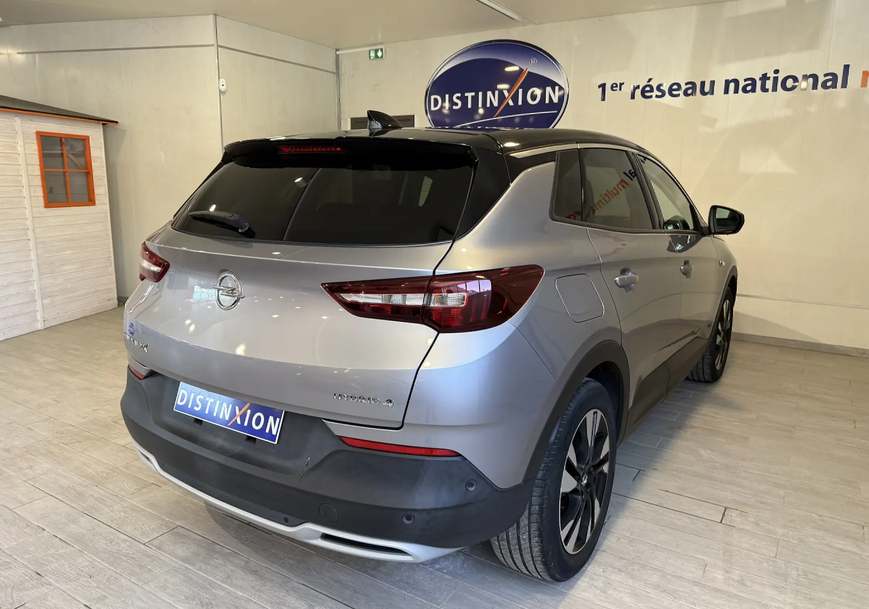 Vue 3/4 arrière droite d'un Opel Grandland X gris Himalaya métallisé avec toit noir et jantes alliage en showroom.