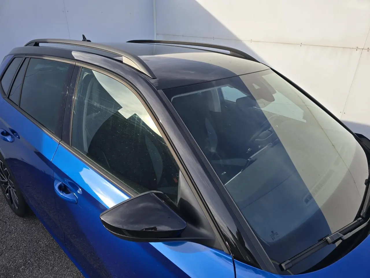 Vue 3/4 avant gauche d'un Skoda Kamiq 2025 bleu racing avec toit noir et barres de toit visibles.