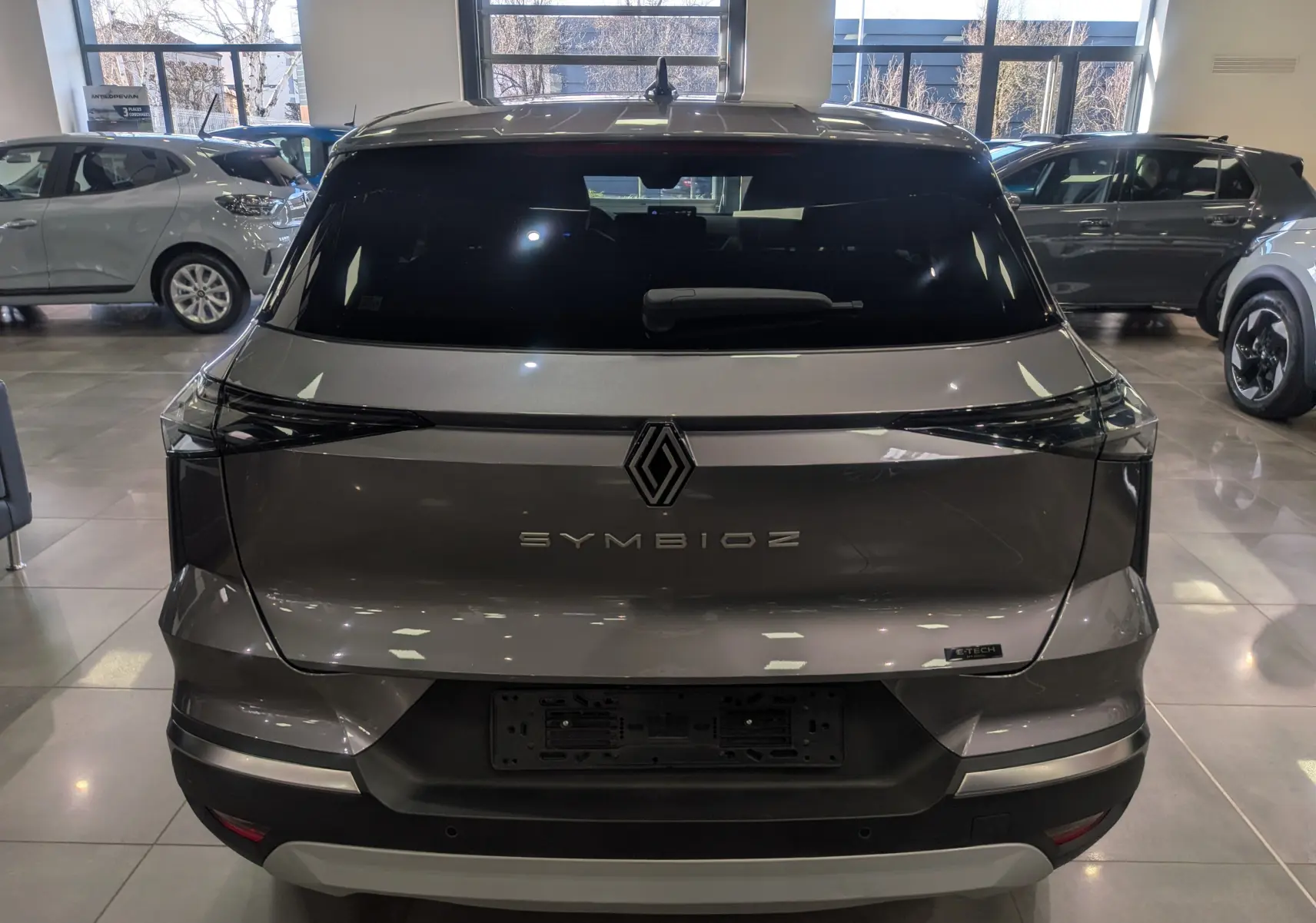Vue arrière d'une Renault SYMBIOZ gris Cassiopé avec logo central et feux arrière étirés en intérieur showroom.