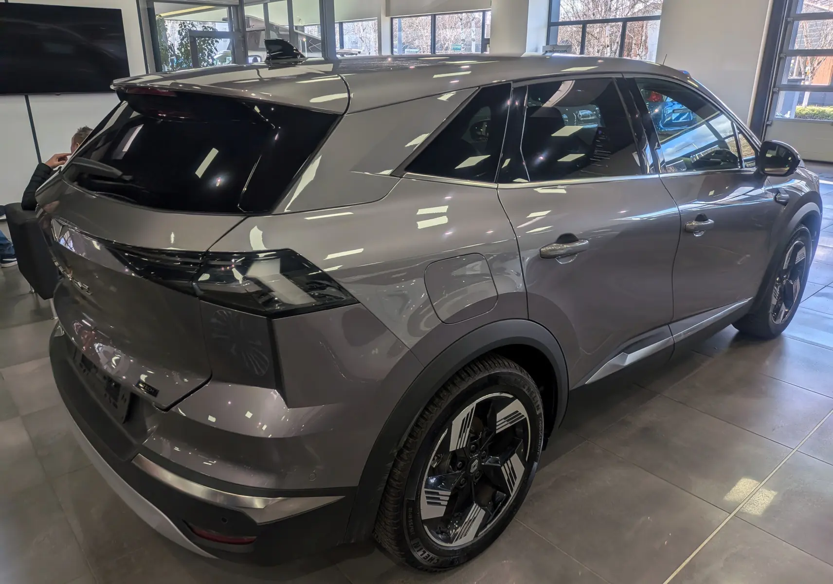 Vue 3/4 arrière droite du Renault SYMBIOZ gris Cassiopé avec jantes bicolores et vitres teintées en intérieur showroom.
