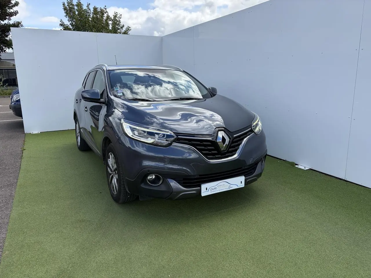 Renault Kadjar gris titanium en 3/4 avant droit, avec calandre chromée et jantes alliage 17 pouces.