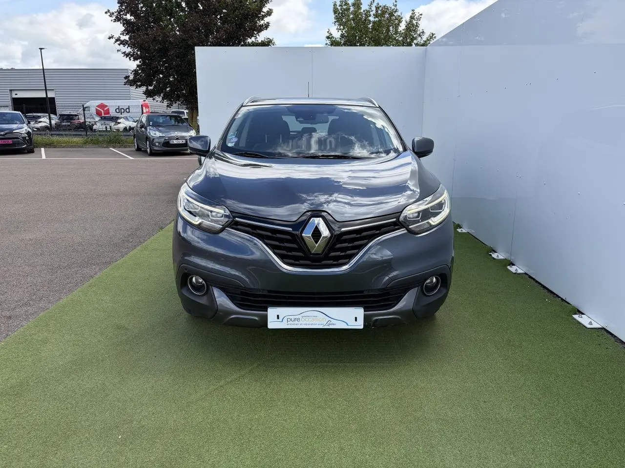 Vue frontale d'un Renault Kadjar gris titanium avec calandre chromée et projecteurs LED sur fond extérieur.