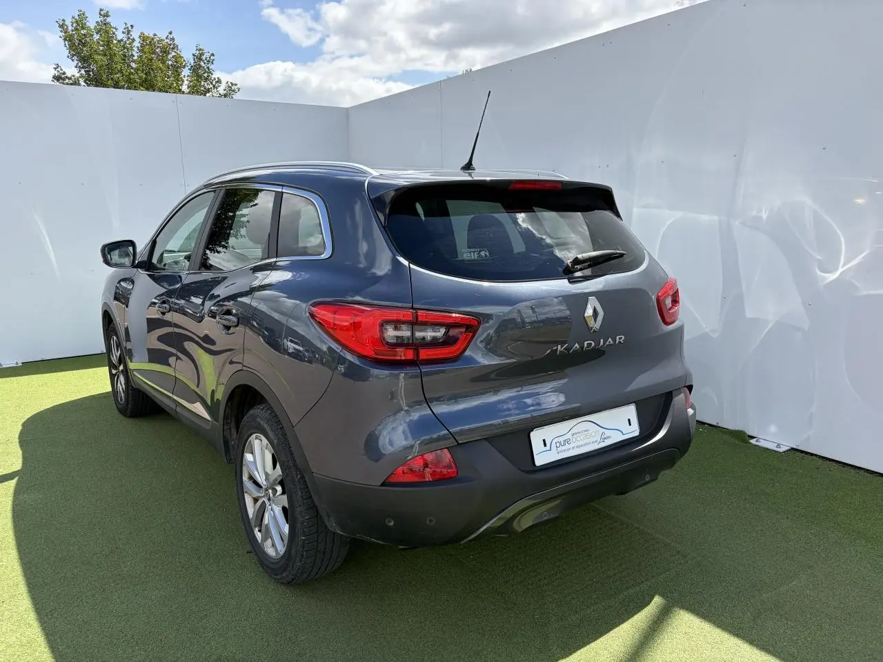 Vue 3/4 arrière droite d’un Renault Kadjar gris titanium avec jantes alliage et feux arrière LED, sur fond clair.