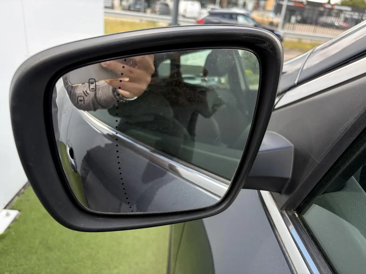 Rétroviseur extérieur côté gauche du Renault Kadjar gris titanium, avec reflet partiel de la portière et du bras du photographe.