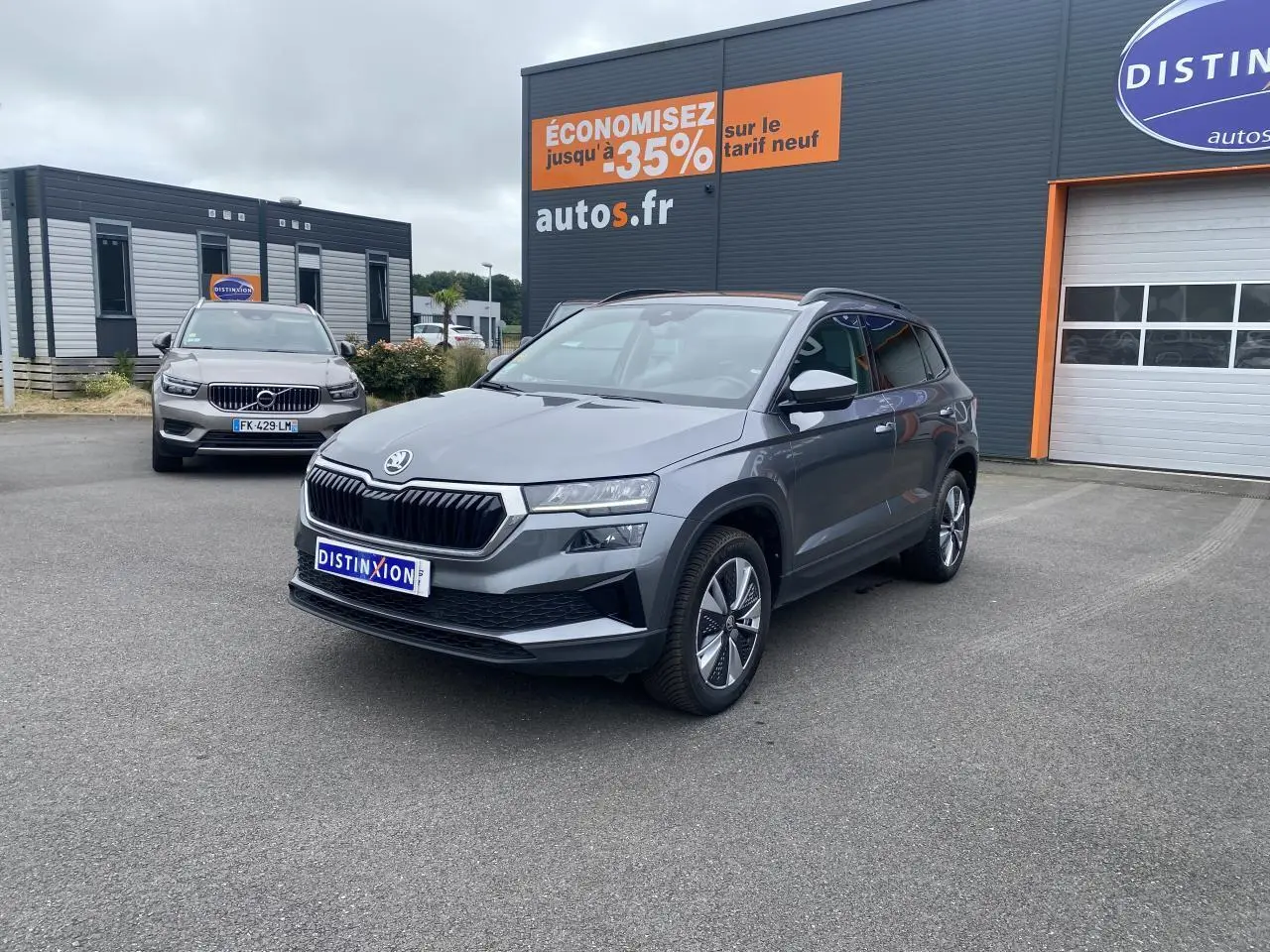 SUV SKODA KAROQ gris graphite métallisé vu en 3/4 avant droit sur parking devant un bâtiment commercial
