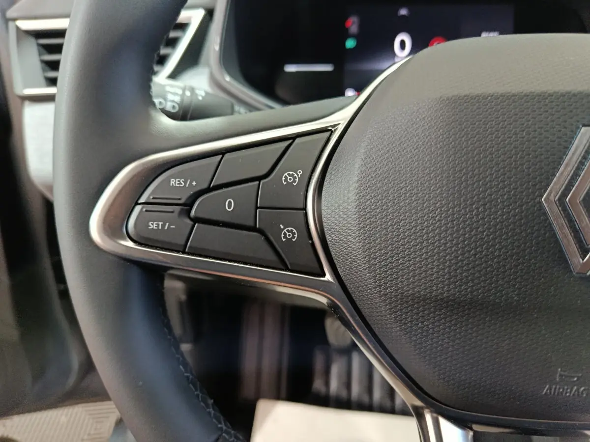 Gros plan sur le volant cuir synthétique gris de la Renault Clio 2025, avec commandes multifonctions et logo central visible.